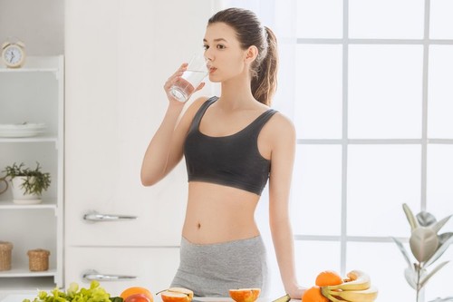 Young female weight loss standing in the kitchen drinking water