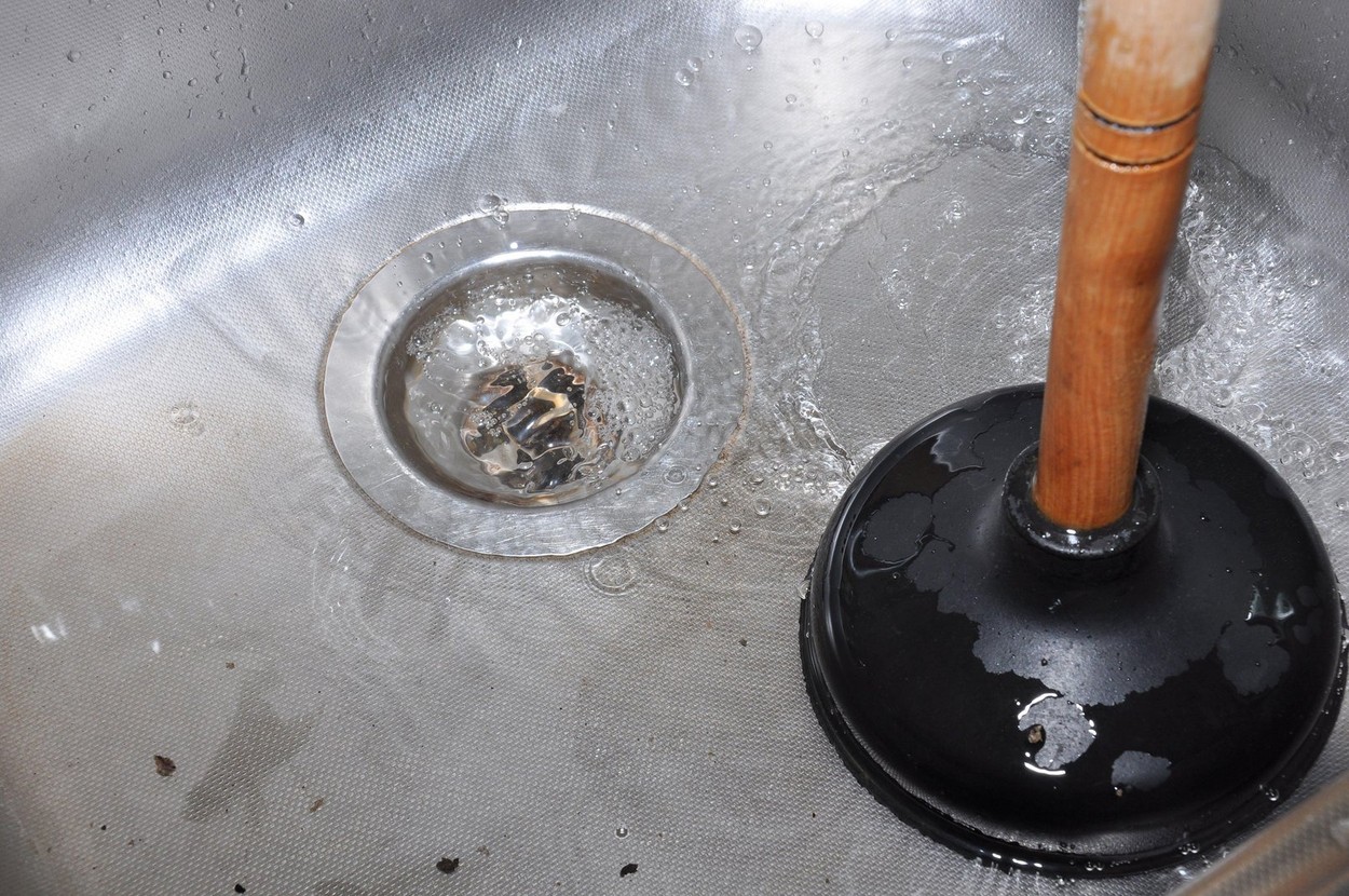 Plunger and clogged kitchen sink. Pipe cleaning concept. Sanitary engineering work.