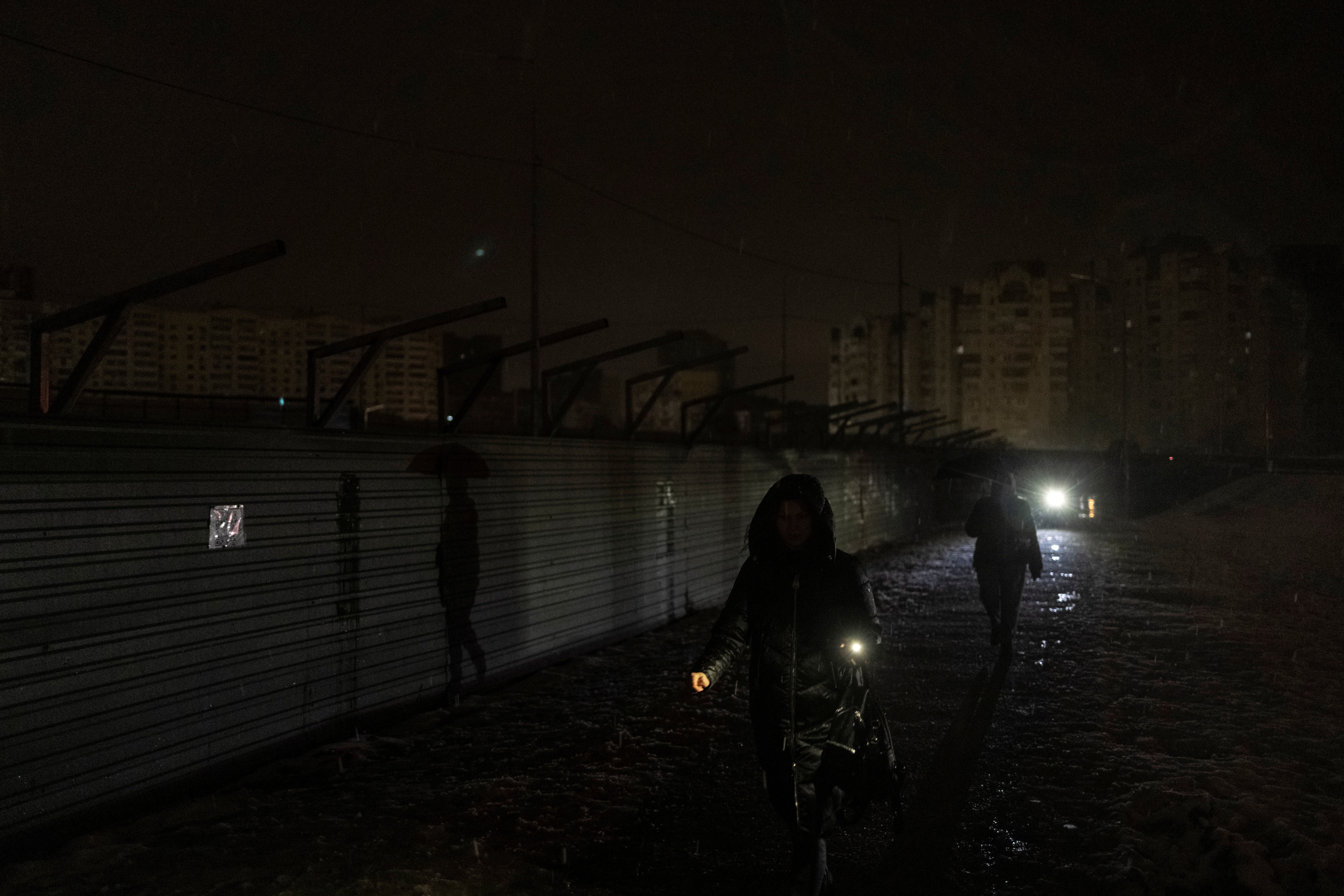 Women walk along a dark street after critical civil infrastructure was hit by Russian missile attacks in Kyiv