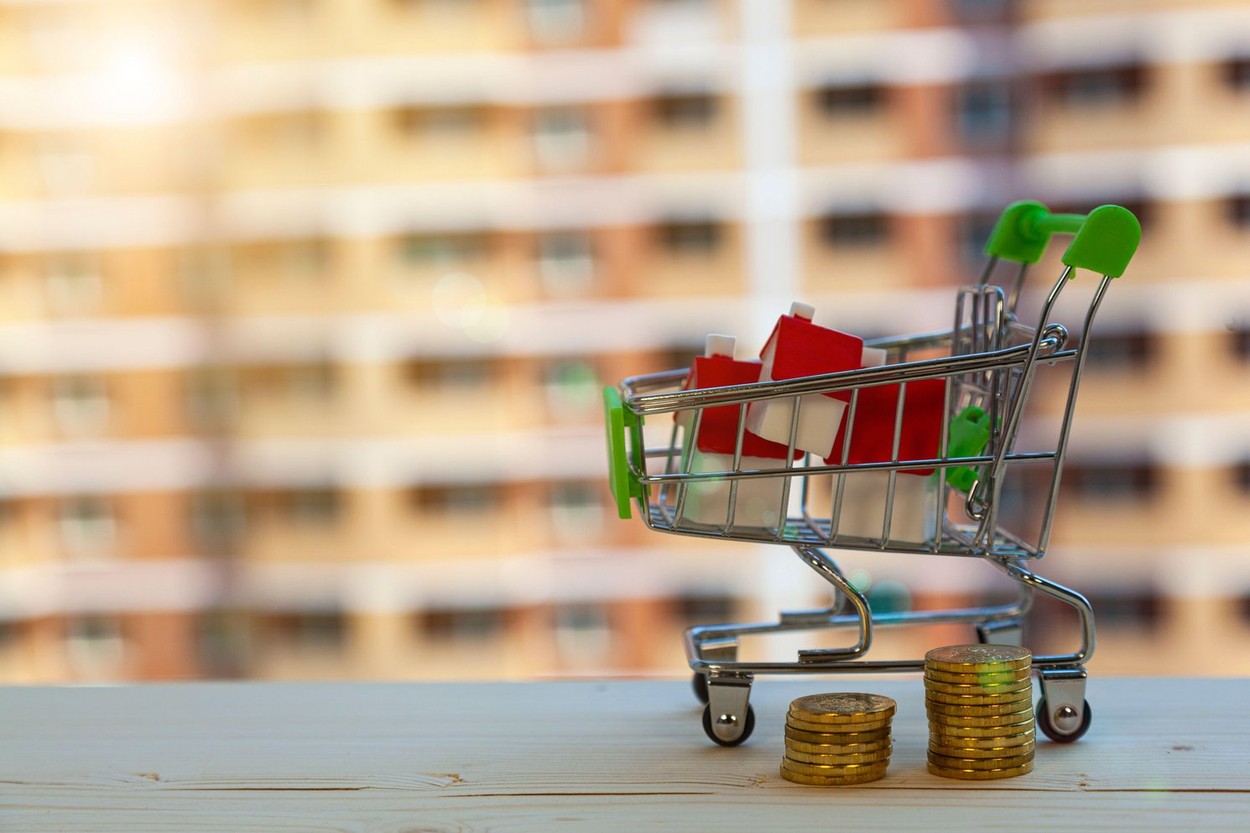 House in a shopping cart and money on the background of a building under construction. Buying a property.