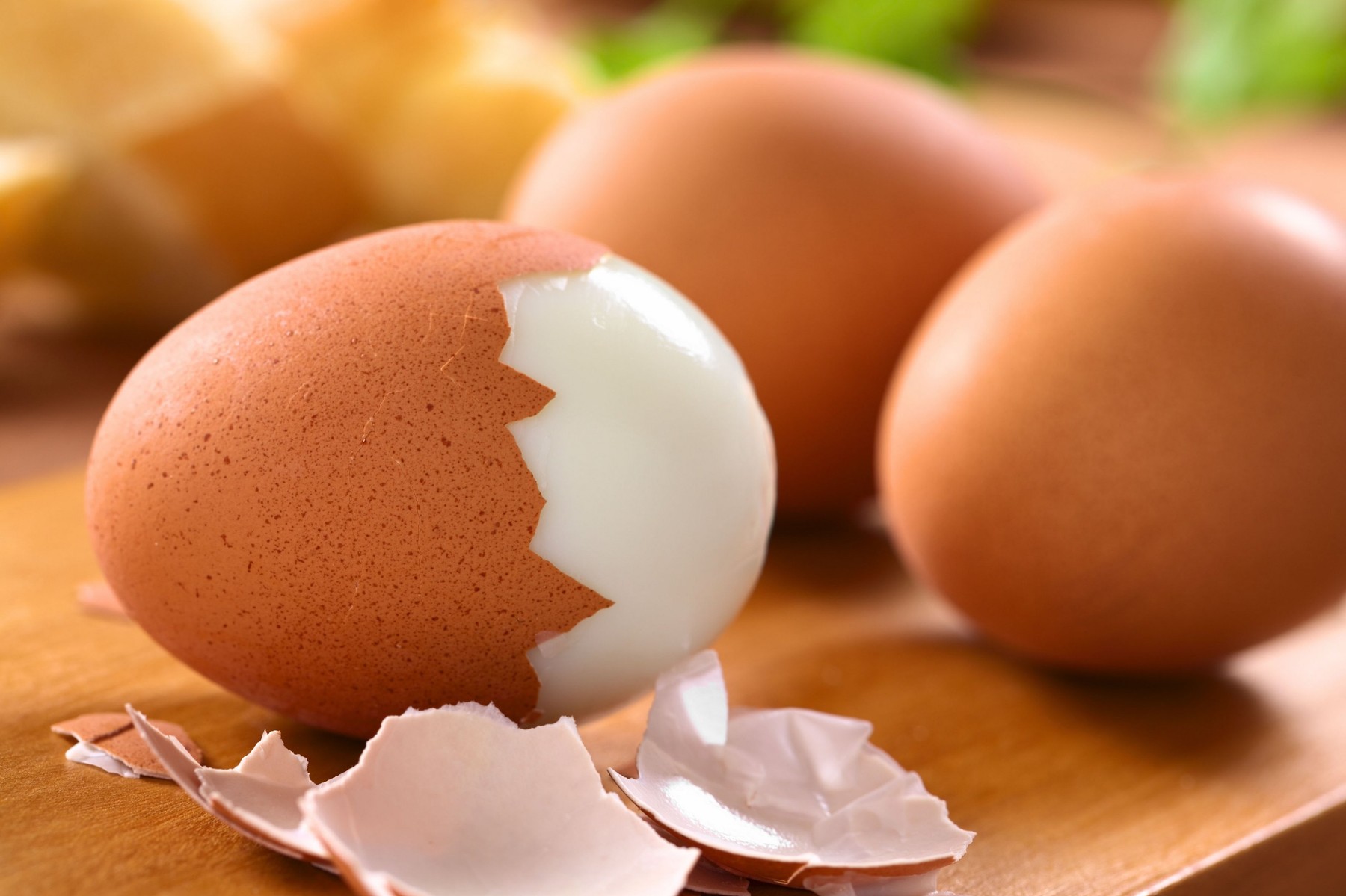Fresh hard boiled eggs with shell beside on wooden board (Selective Focus, Focus on the front of the shell on the first egg)