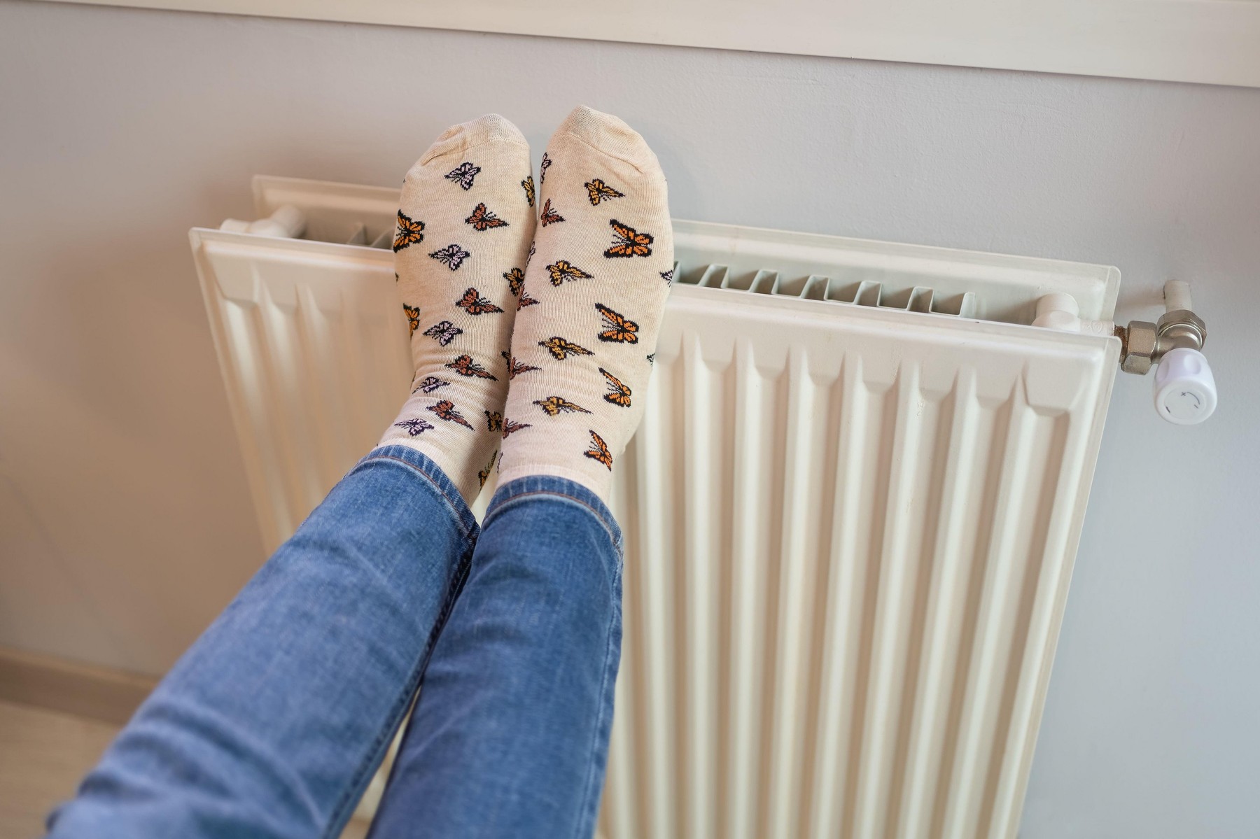 Woman with her feet resting on a radiator to warm them up due to the cold of winter.