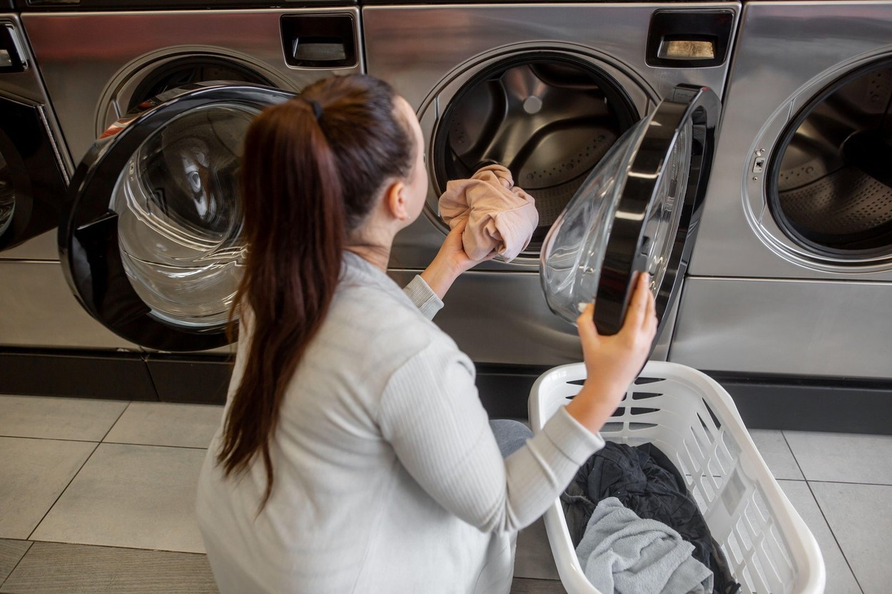 Pretty young woman putting, getting some dirty clothes into a washing machine in a laundry, laundry cleaning