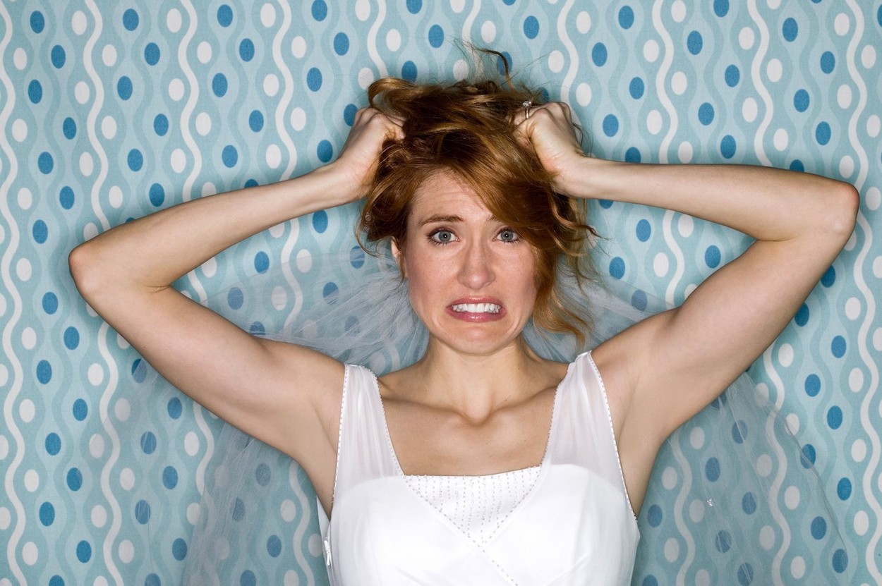 Bridezilla bad hair day, studio portrait of woman in wedding dress pulling her red hair.