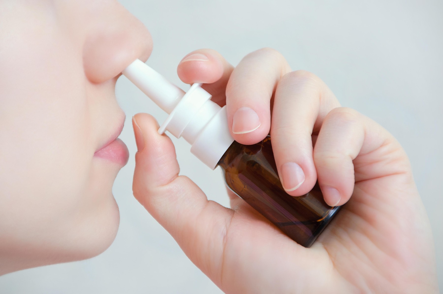 Nasal spray.  Beautiful young woman. Face with nasal drops. Close-up of female spraying medical nasal spray in her nose. Cold and flu, health care con