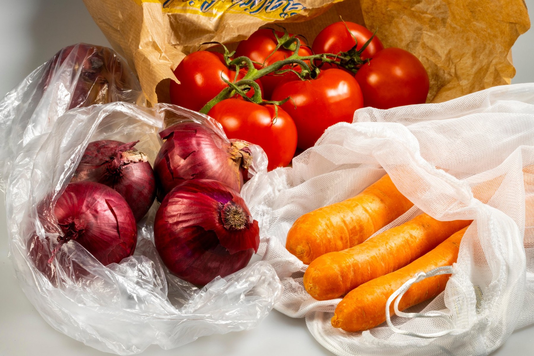 Food packaging, carrots in a reusable plastic net, avoiding plastic garbage, onions in a disposable plastic bag, tomatoes in a paper bag,