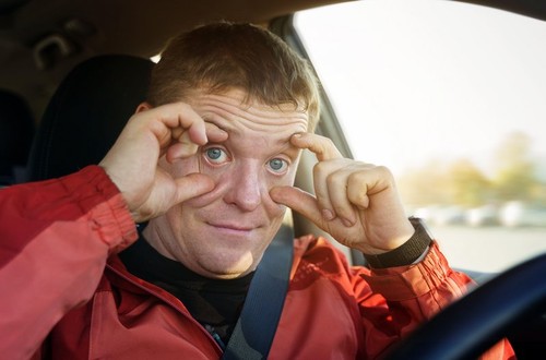 A tired driver holds his eyelids with his fingers, preventing them from closing while sitting at the wheel while driving. Security concept.