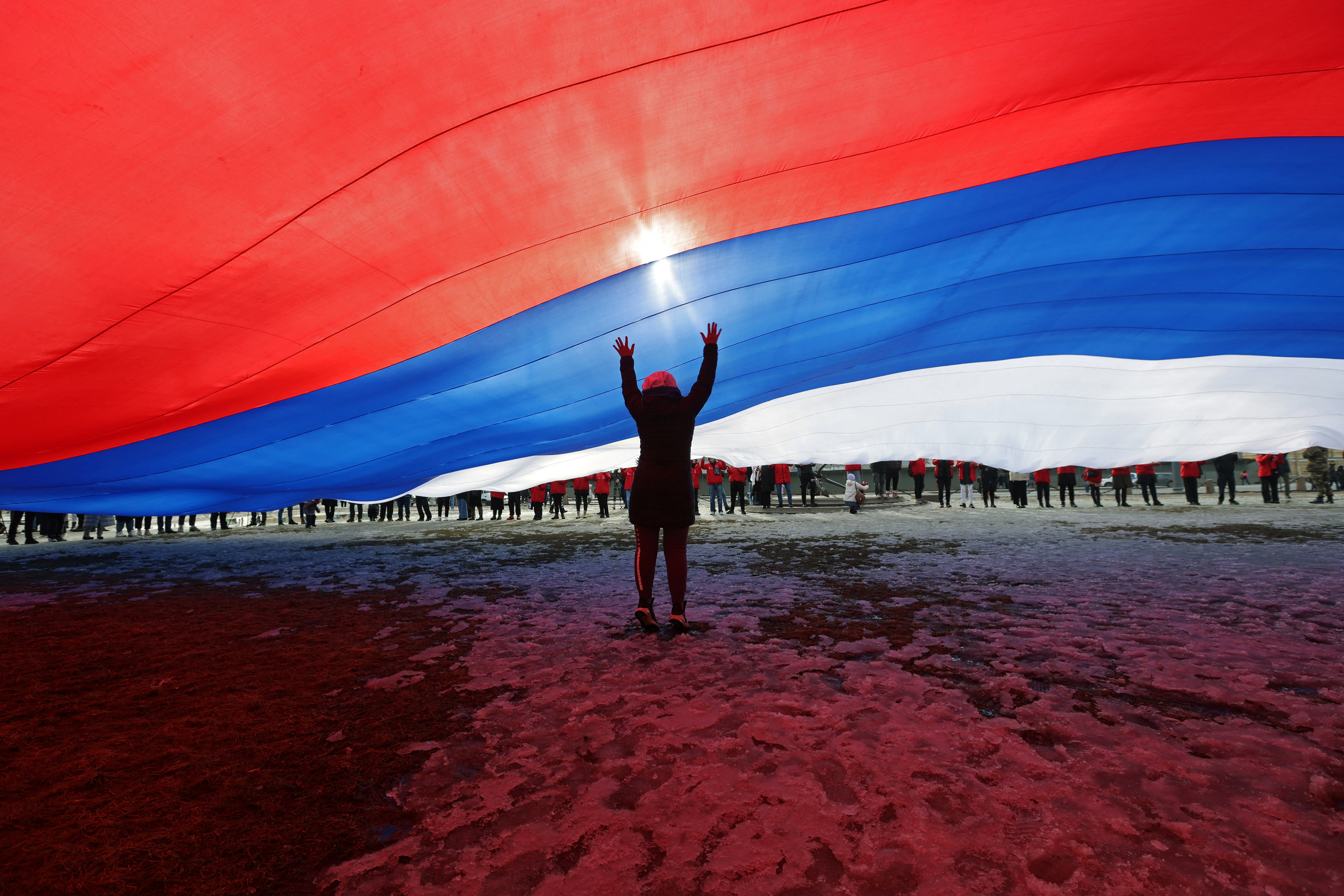 A participant stands under a giant Russian national flag during an event marking the ninth anniversary of Russia's annexation of Crimea, in Saint Petersburg
