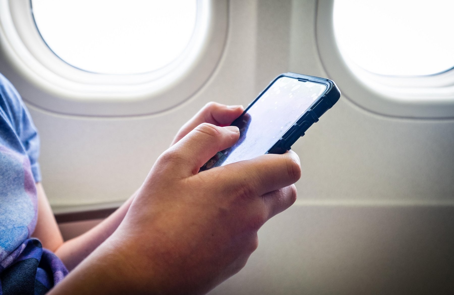 A teenage boy using his mobile phone during the flight on a plane