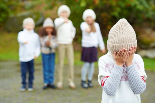 Little boy crying with his face in hands on background of bullying children
