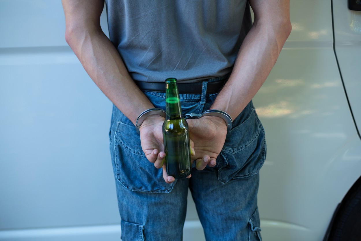 Midsection of man with handcuffs holding beer bottle