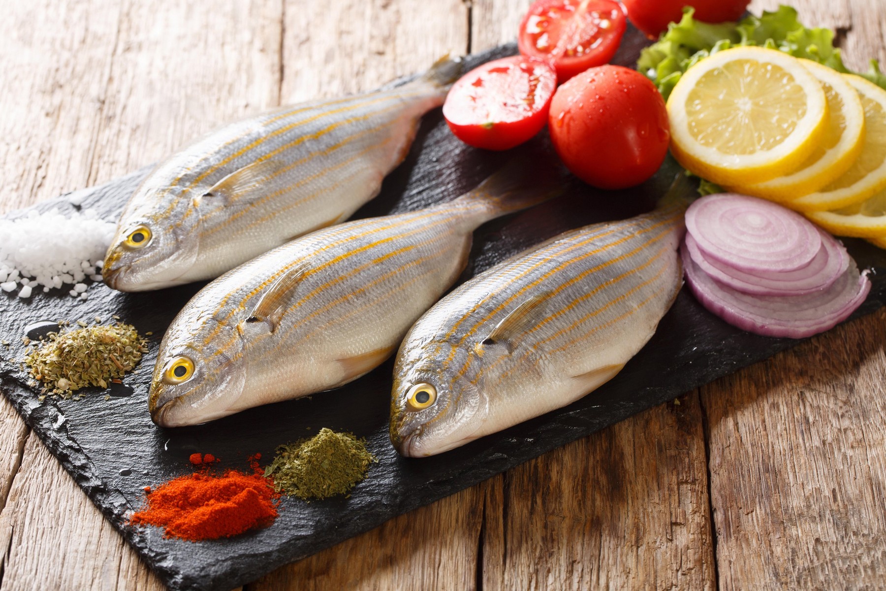 Healthy raw Sarpa salpa with fresh vegetables and spices close-up on a slate board on the table. horizontal