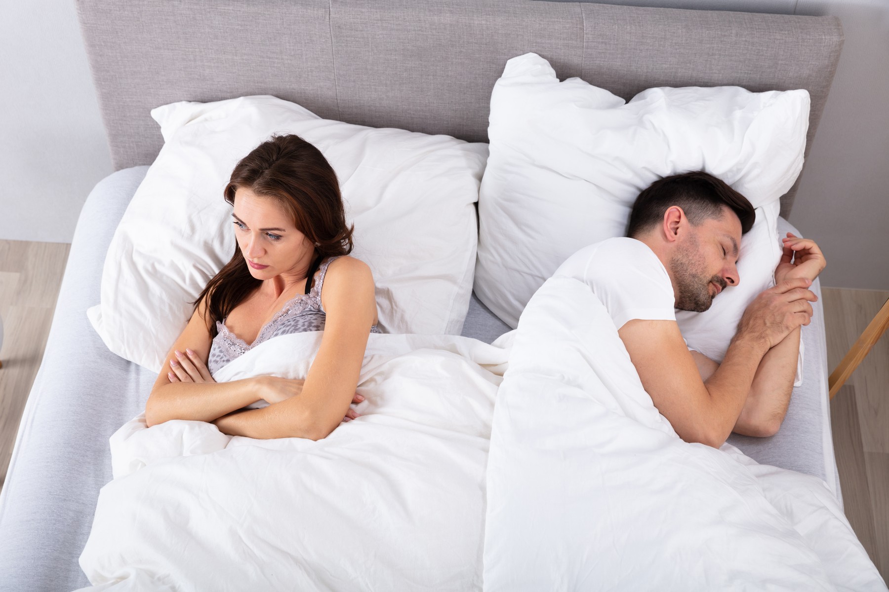 Woman Lying On Bed With Her Husband Sleeping At Home