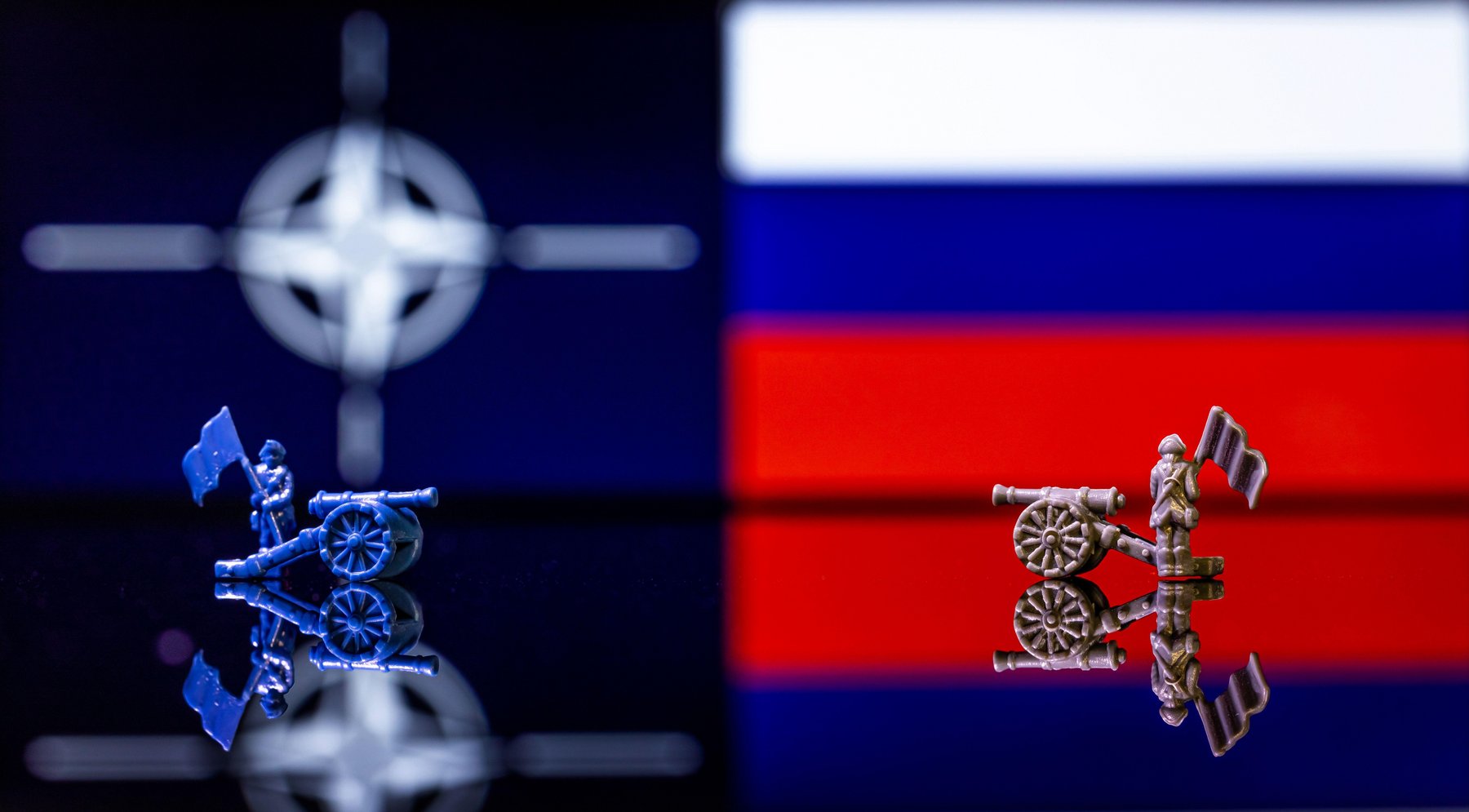 Conceptual image of war between Russia and NATO using toy soldiers and national flags on a reflective background