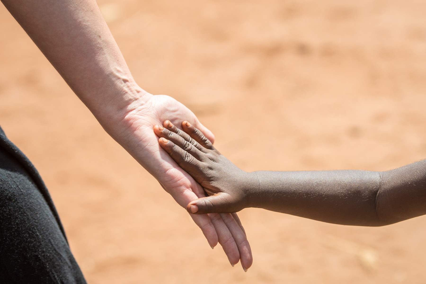Hand of young Zambian child lightly placed against adult Caucasian woman, Mukuni Village, Zambia