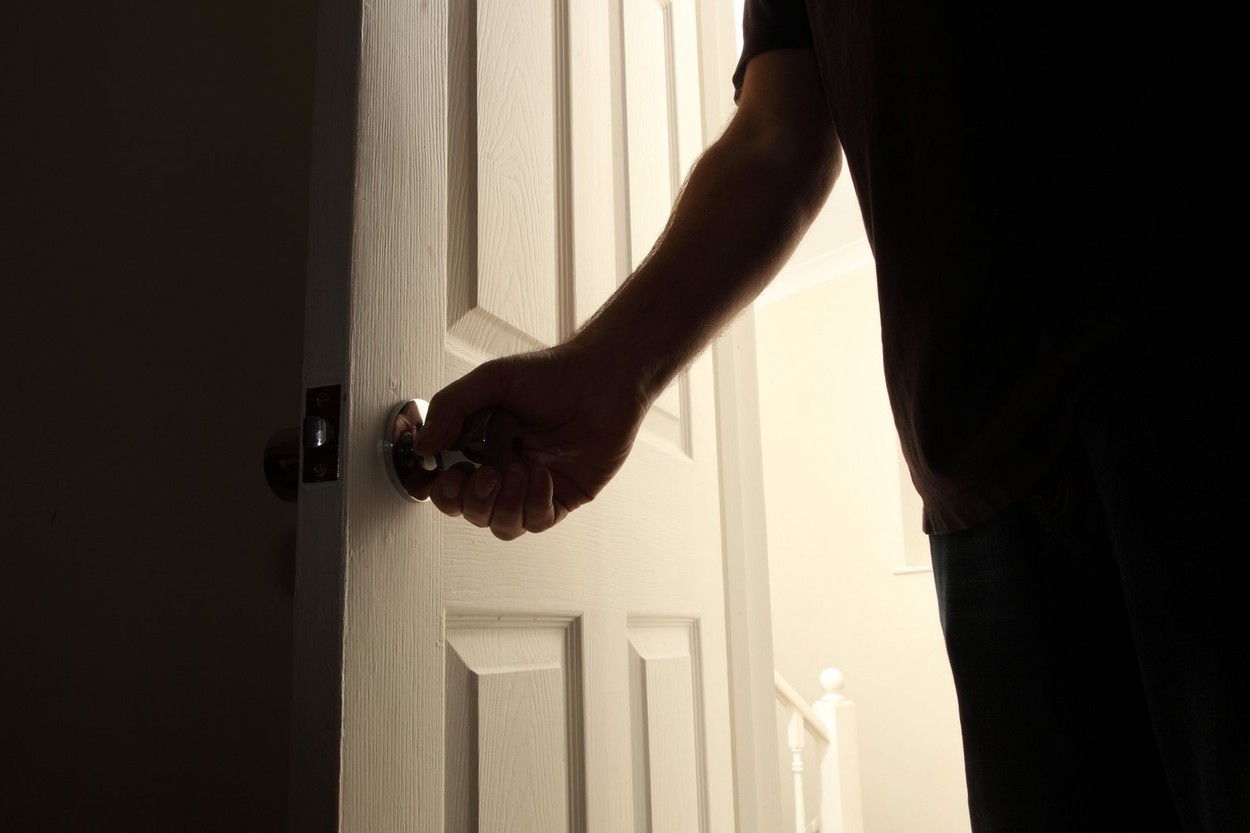 Man's hand opening a door to a dark room at night