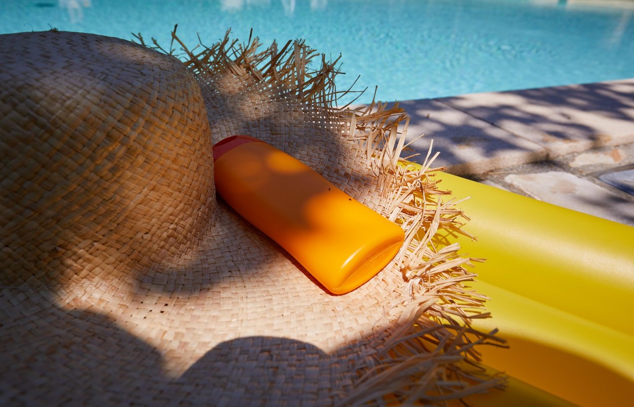 Hat and bottle of sun cream by the pool