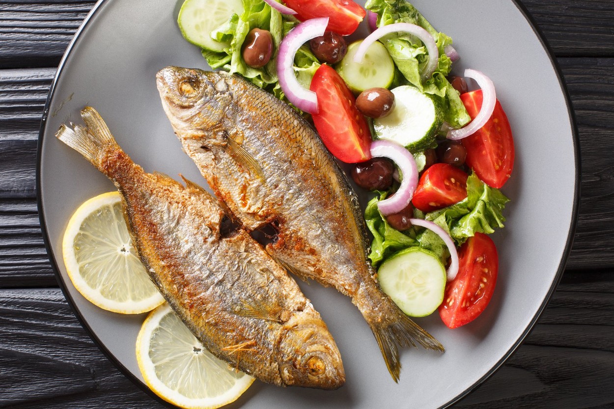 Delicious fried salpa fish with fresh vegetable salad close-up on a plate on the table. horizontal top view from above