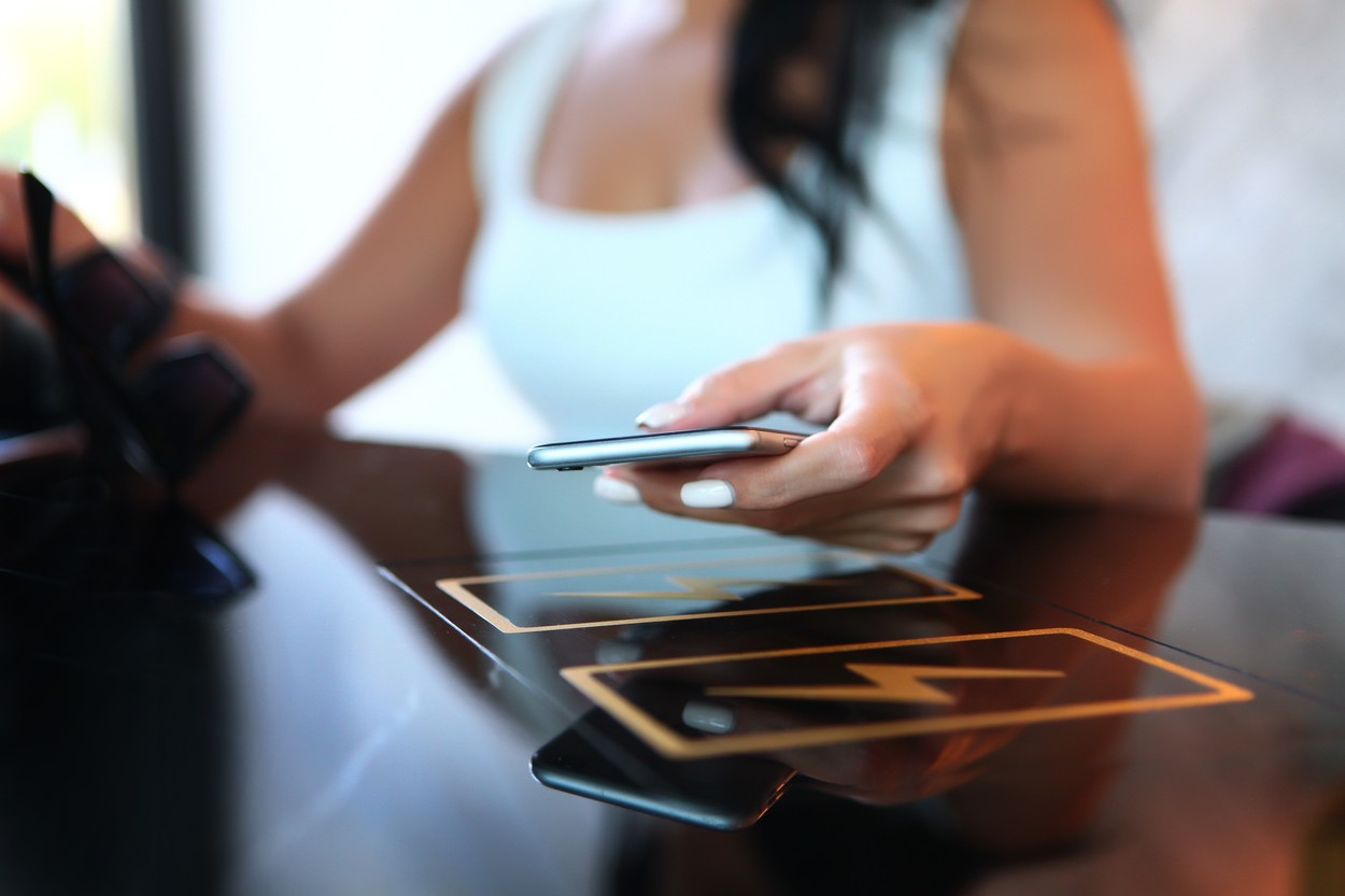 Wireless charging of your phone or gadget in a public place or in a cafe. A woman's hand is holding a phone. Unrecognizable person. Dark background. Copy space.