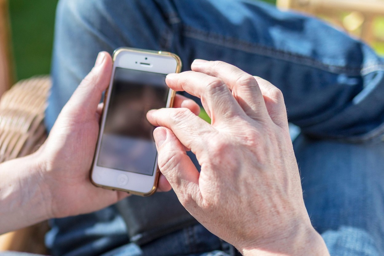 Senior, mature man using mobile smart phone outdoor in the garden while relaxing in the summer sun in a UK garden