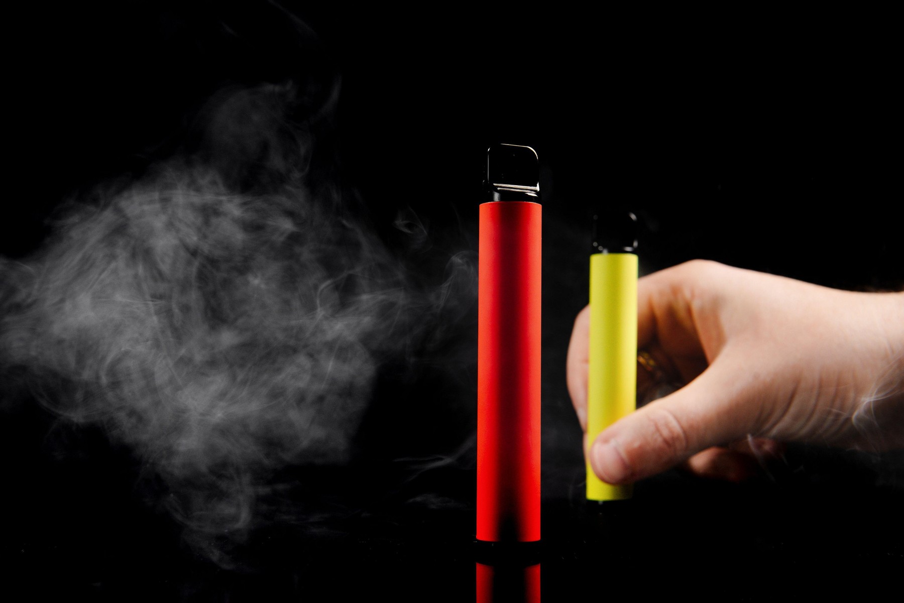 Disposable electronic cigarettes of different flavors in hand on a yellow background. The concept of modern smoking, vaping and nicotine.