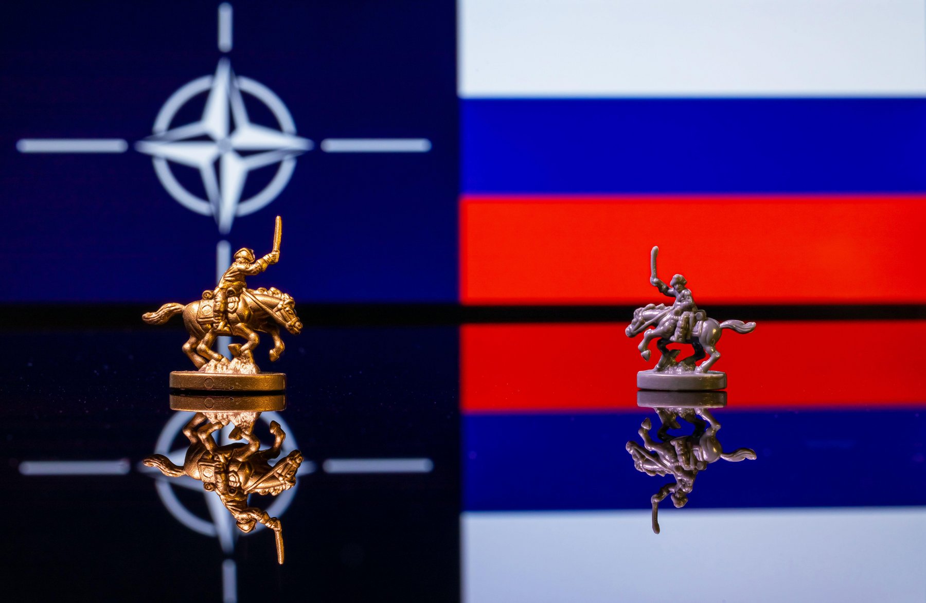 Conceptual image of war between Russia and NATO using toy soldiers and national flags on a reflective background