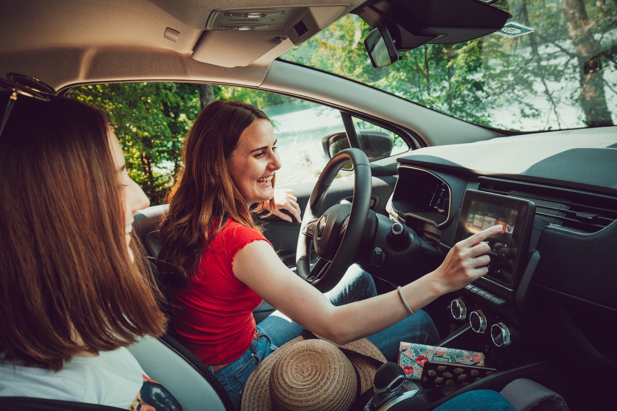 Two young female friends driving, listening to good music in car, enjoy road trip in summer.