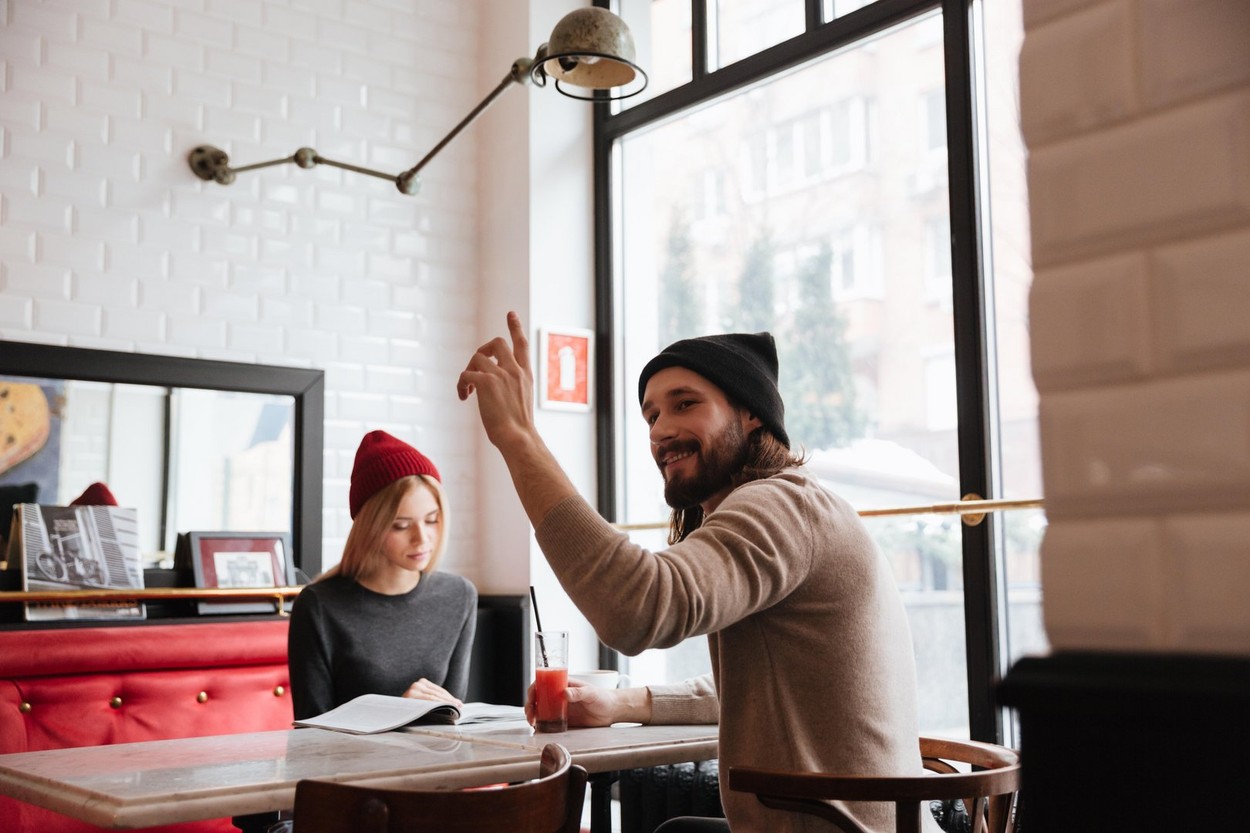 Woman with man sitting by the table in cafe and man calling the waiter
