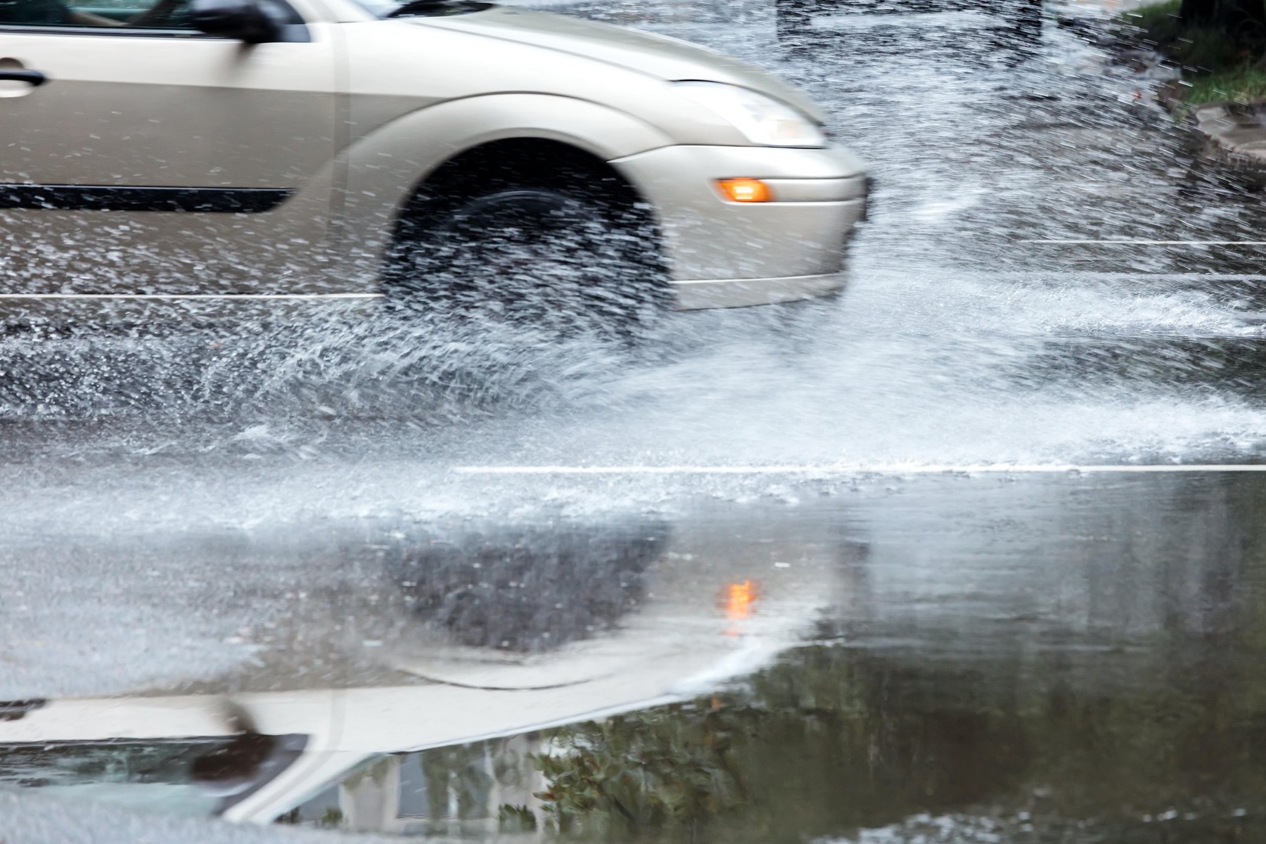 car in motion on flooded road reflecting in water puddles during rain