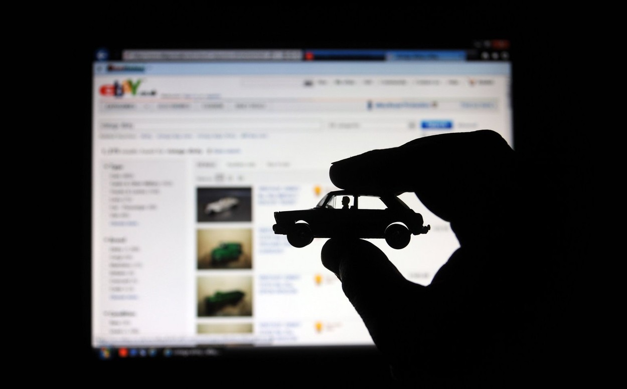 MODEL CAR HELD IN MANS HAND WITH COMPUTER SCREEN WITH EBAY AUCTION SITE BEHIND RE INTERNET SHOPPING SELLING BUYING BUSINESS UK
