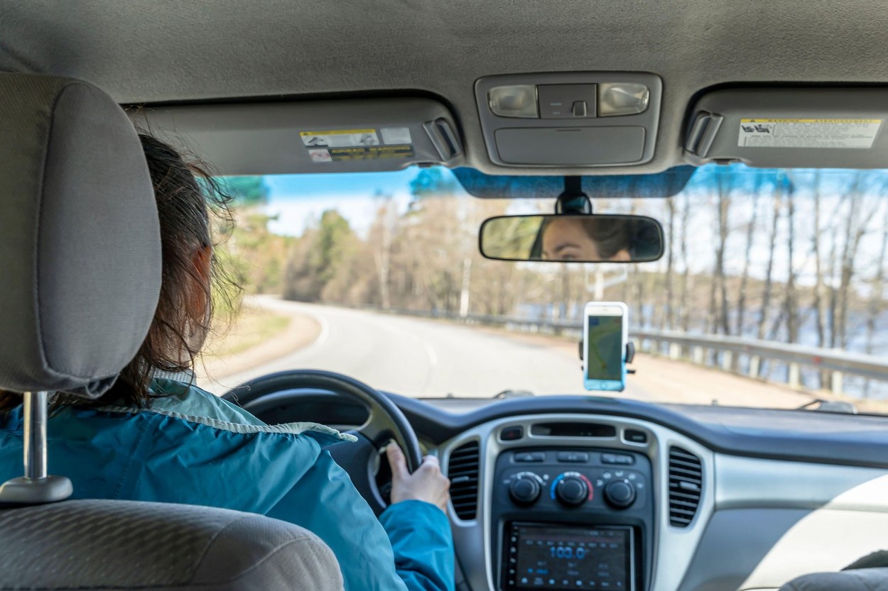 caucasian middle-aged woman driving a car on the highway. A view from the back of a woman driving a car. The driver's hands hold the steering wheel an