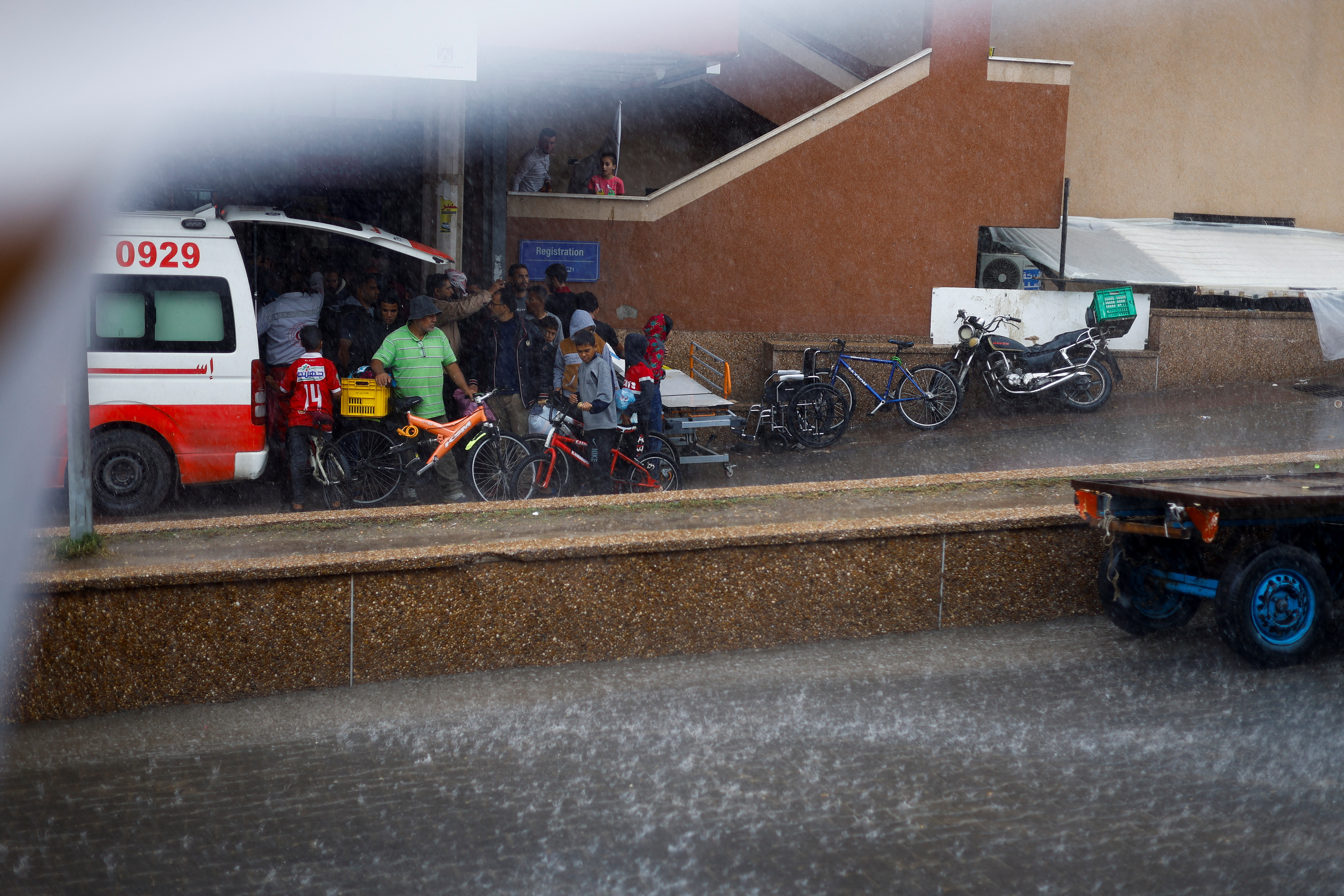 Palestinian stand next to an ambulance during a rainfall, amid the ongoing conflict between Israel and Palestinian Islamist group Hamas, outside the hospital in Khan Younis