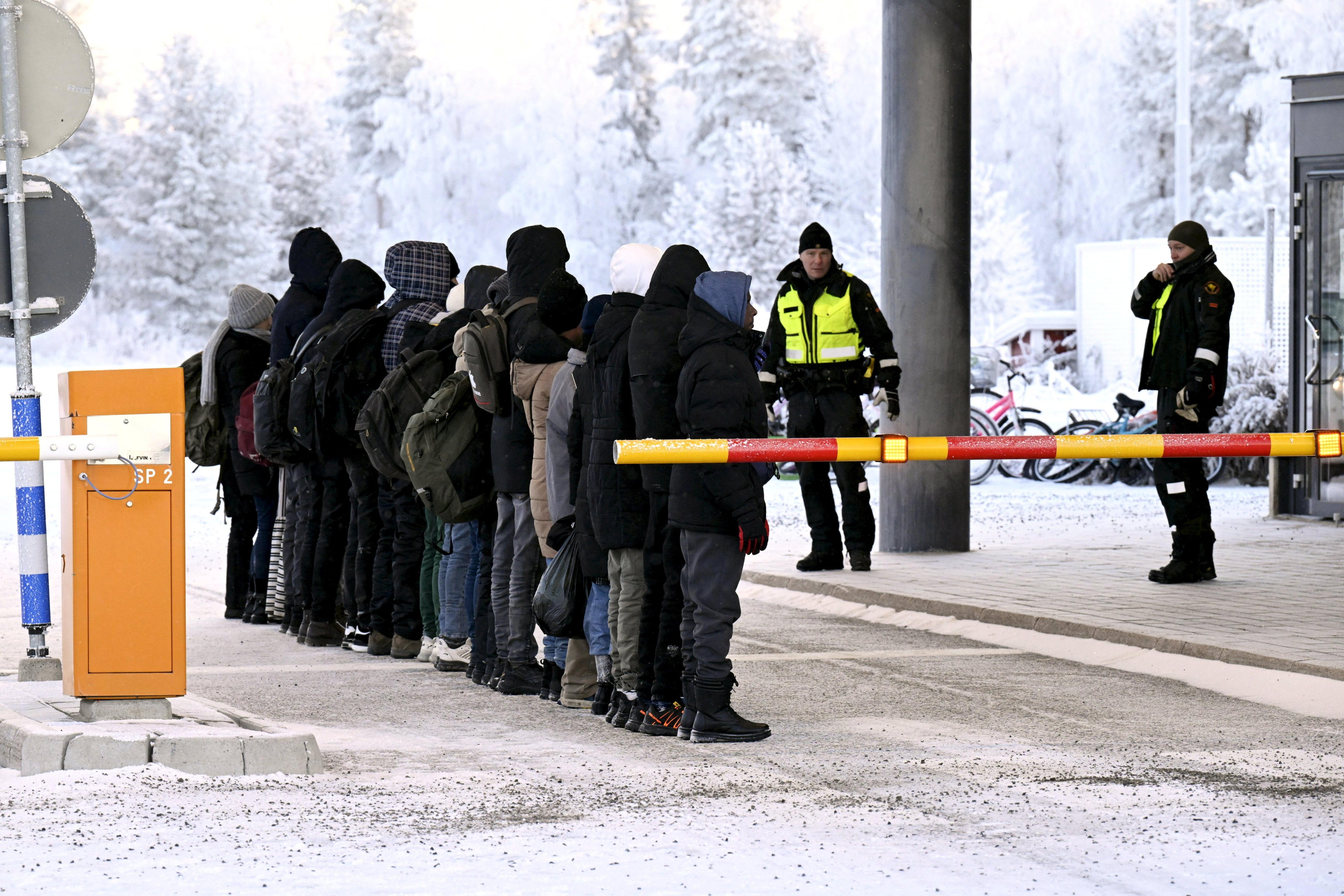 Migrants are lined up in front of Finnish Border Guards at the international border crossing at Salla