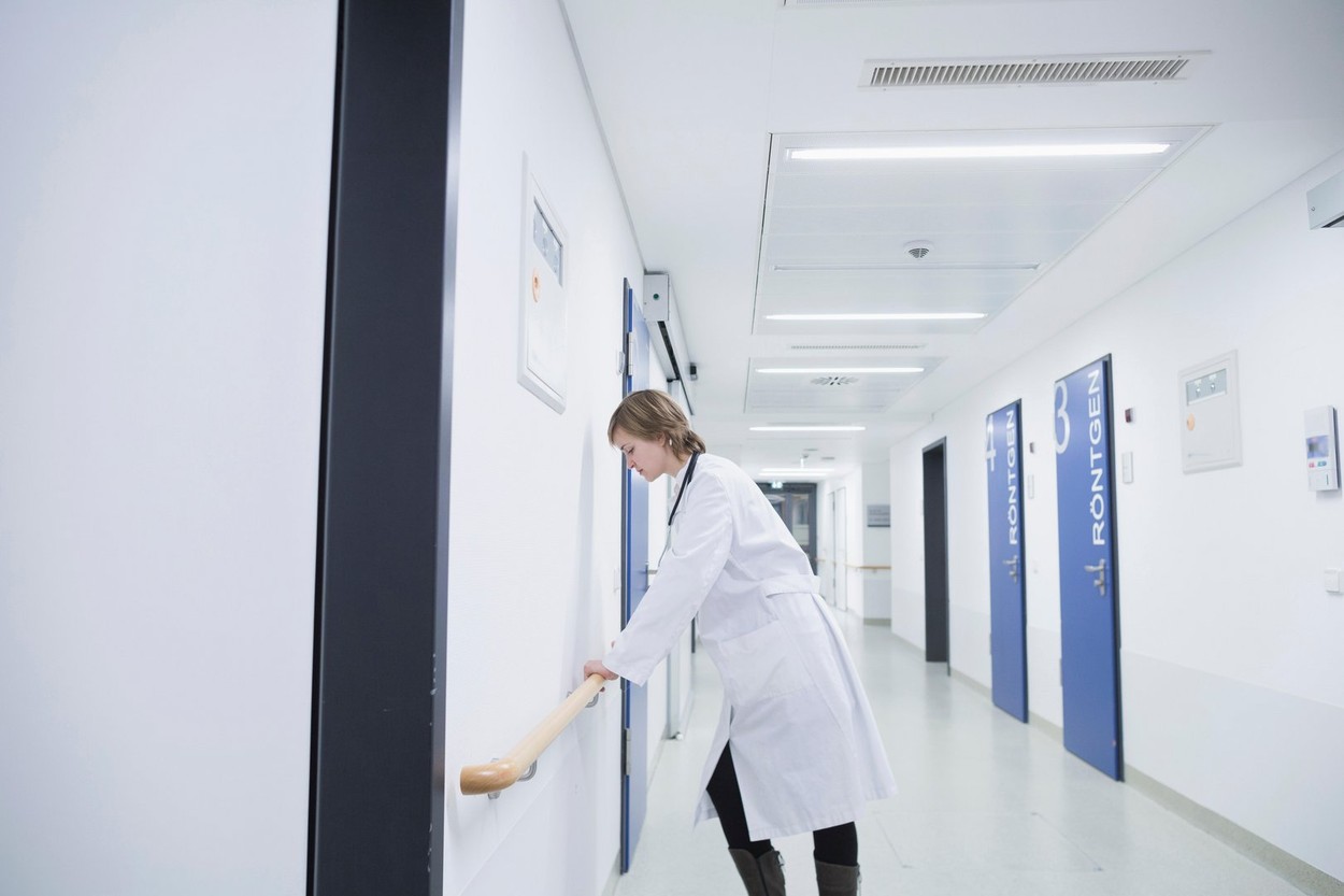 Side profile of overstressed young female doctor leaning against railing in hospital corridor, Freiburg Im Breisgau,