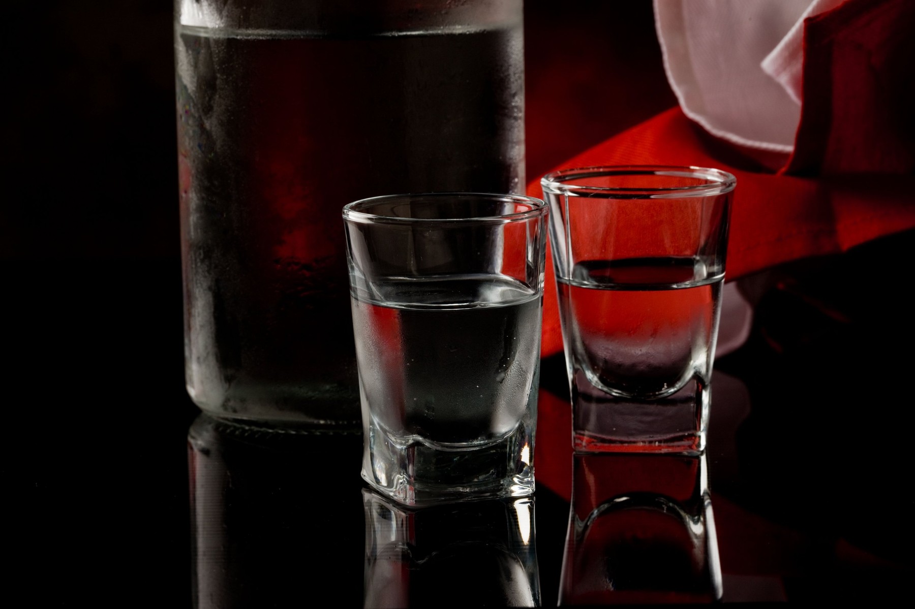 photo of cold vodka bottle with glass on black glass table