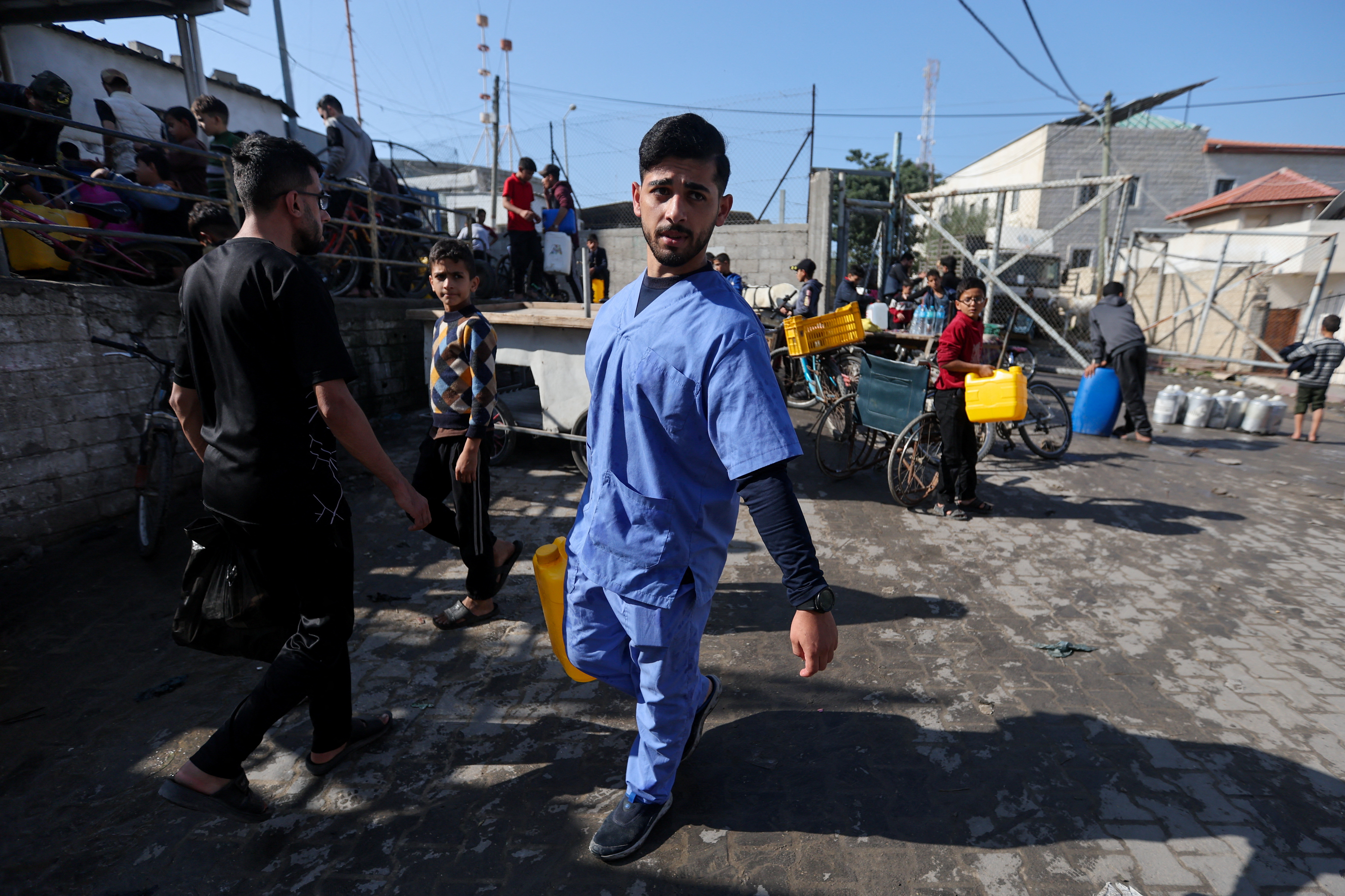 Nurse displaced from Gaza's Al-Shati refugee camp walks with water can in Khan Younis