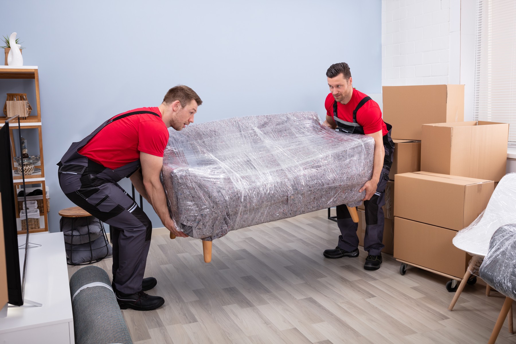 Male Movers Carrying Wrapped Sofa In New House
