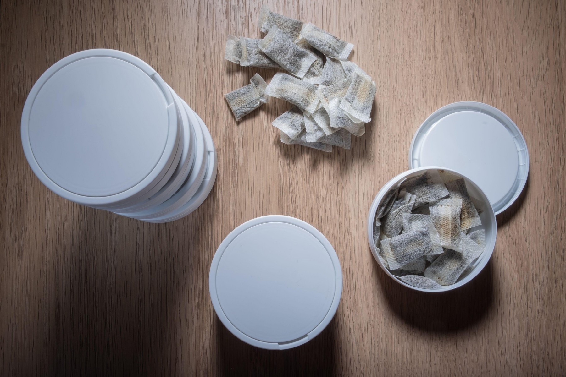 Helsinki / Finland - JUNE 9, 2022: Studio shot of white Swedish smokeless tobacco cans and portion snus pouches on a wooden table.