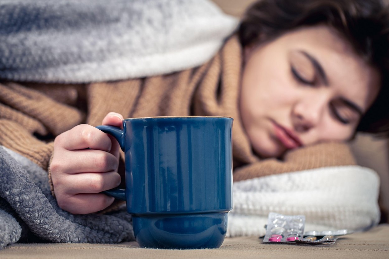 Young woman lies in bed with a cup of drink, home treatment, colds.
