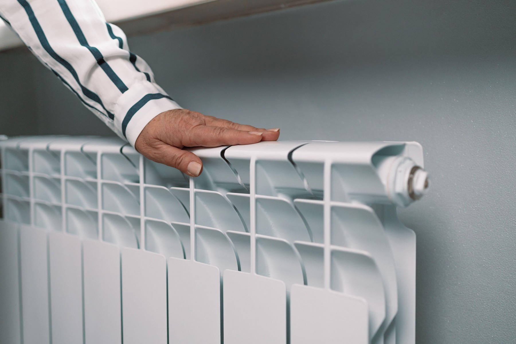 Female hand touch a heating radiator at home.