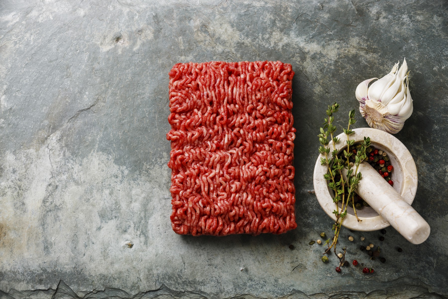 Minced meat forcemeat on stone slate background with pepper, gar
