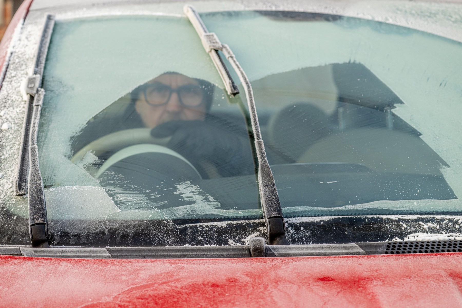Closeup of a partially cleared frozen car windscreen with a male driver sitting inside. UK