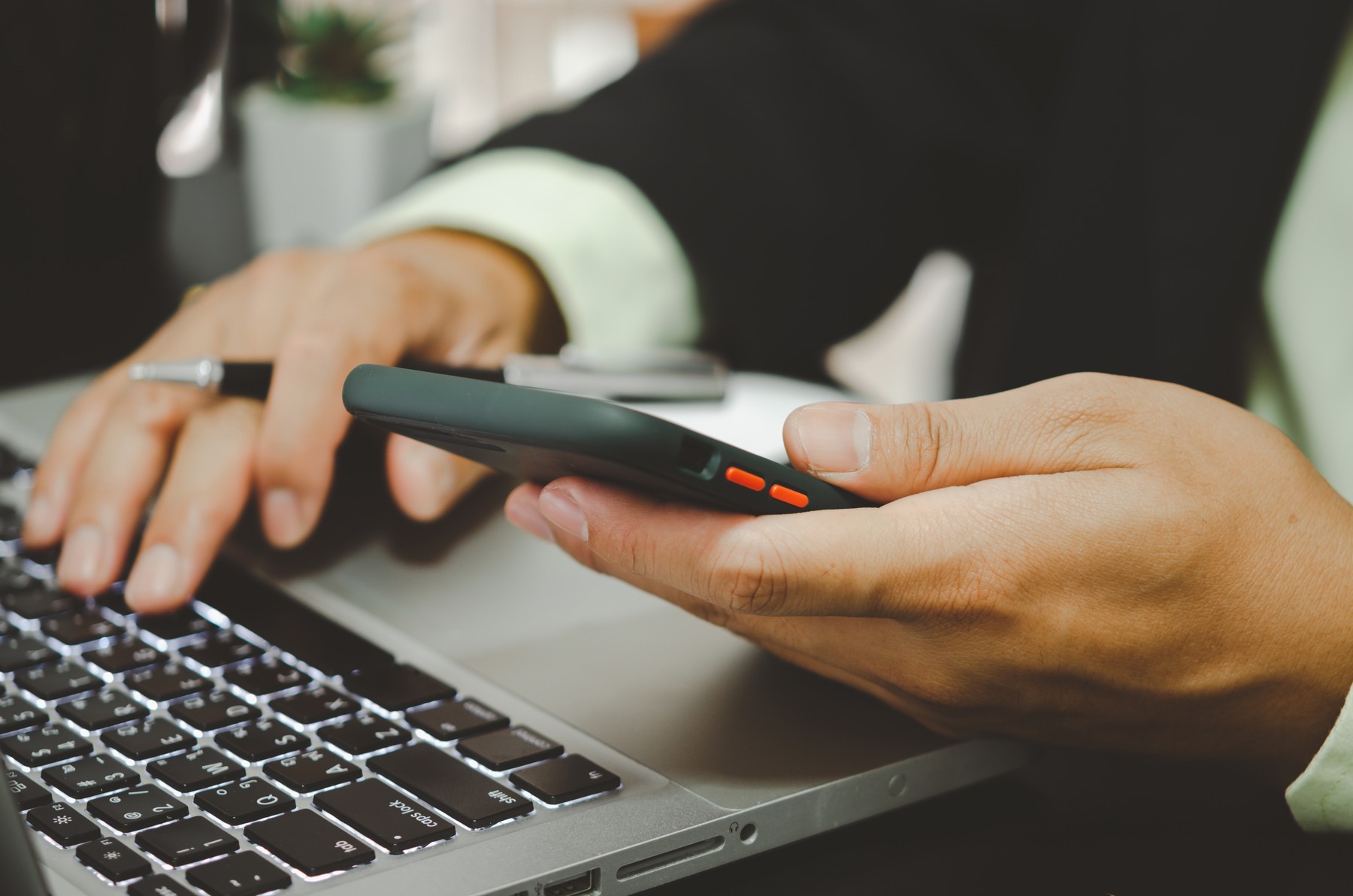 hand business man holding a mobile phone and typing on a computer keyboard.