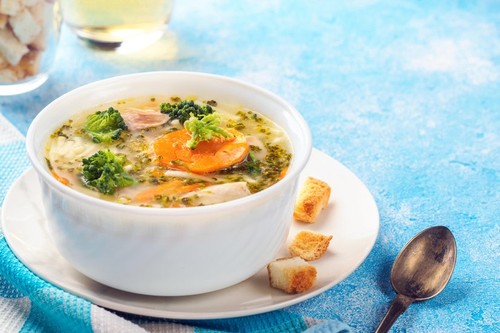 Italian vegetable soup with broccoli carrots noodles in chicken broth on blue table with slices of bread and glass juice. Food vegetarian organic stil