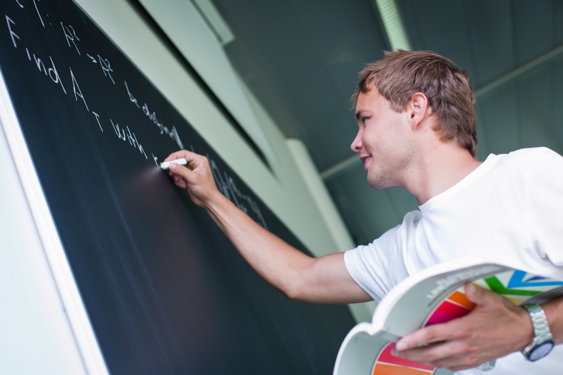 handsome college student solving a math problem during math class in front of the blackboard/chalkboard (color toned image)