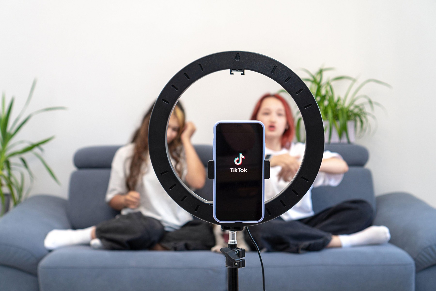 Two white teenage girls shoot a viral video on their channel in the social network Tiktok at home on the couch. Focus on Tik Tok logo. Turkey, Istanbu