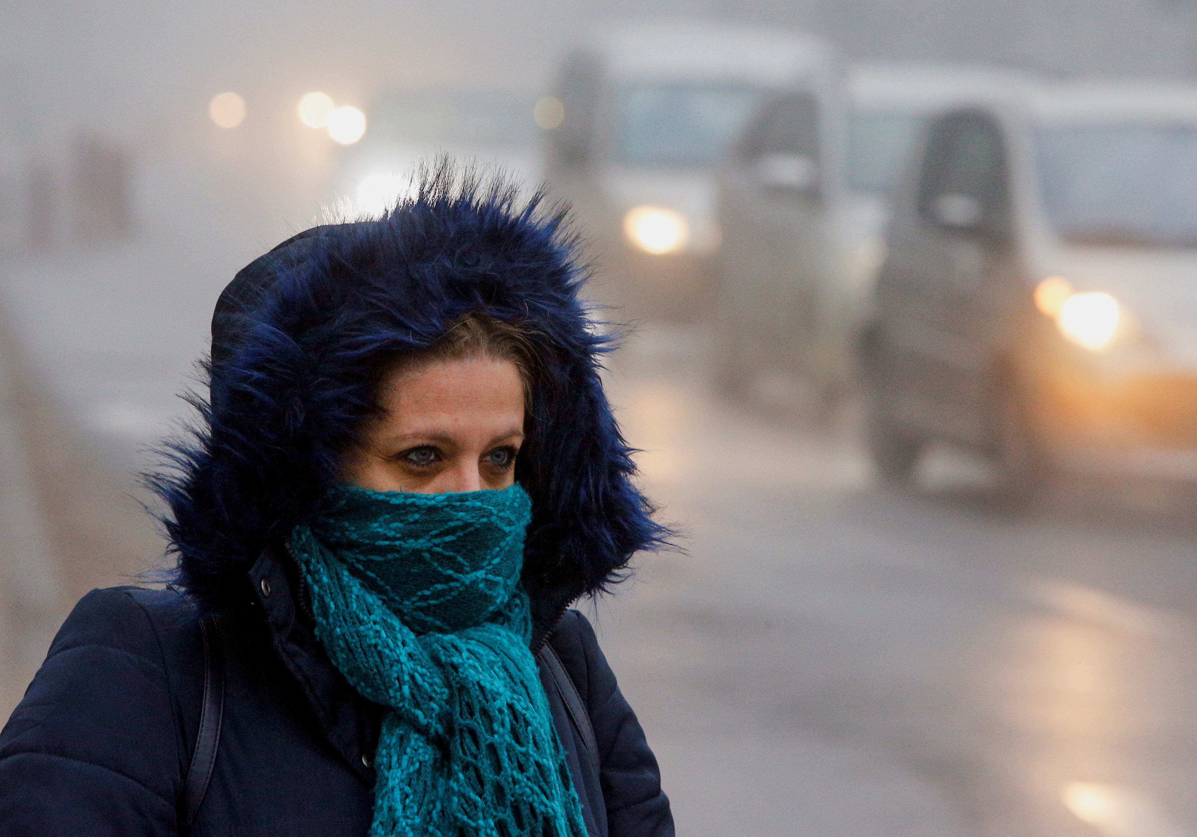 A woman wearing a mask walks as fog blankets the city of Skopje
