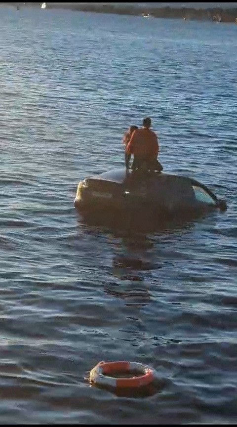 A view shows people on top of a partially submerged car in the Oslofjord, in Oslo