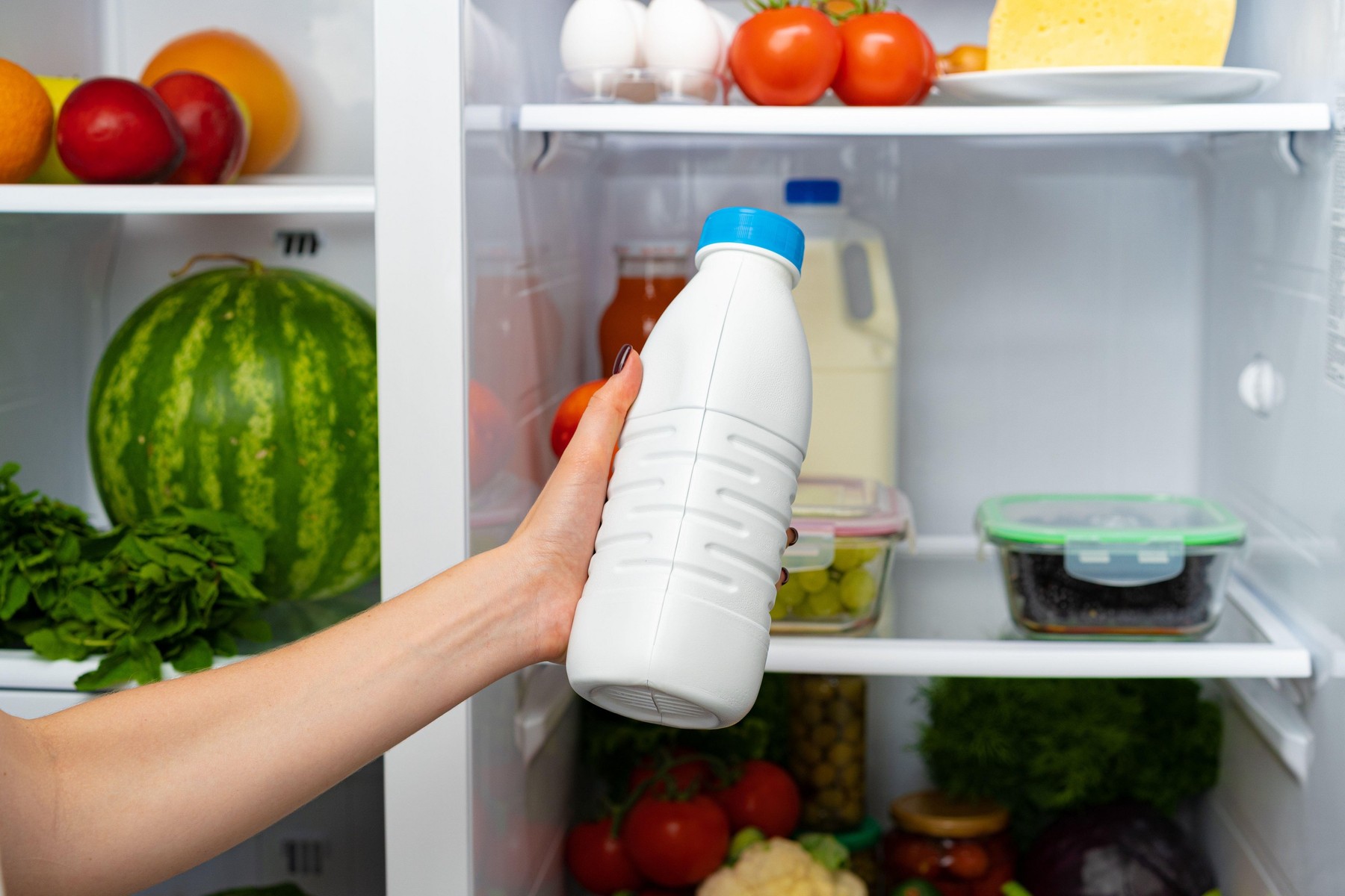 Female hand taking bottle of milk from a fridge