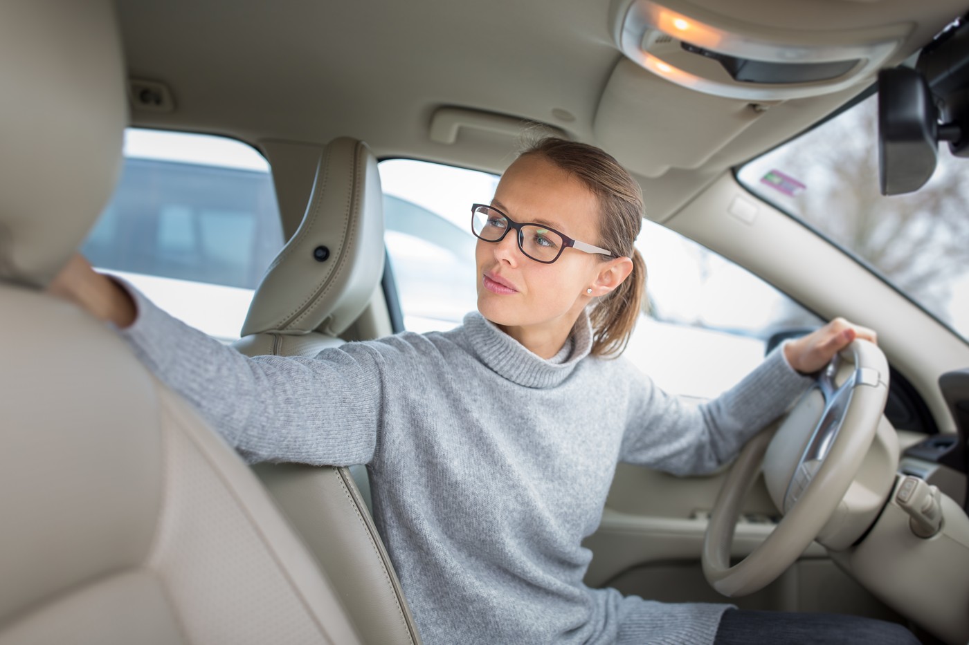 Woman driving a car - female driver at a wheel of a modern car, parking, going in reverse using the parking sensors